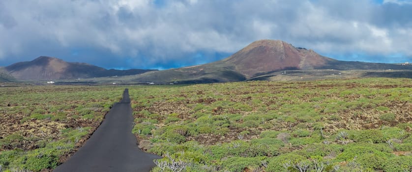 A winding road through lush greenery leads to a distant volcano under a dramatic sky, embodying isolation and adventure.