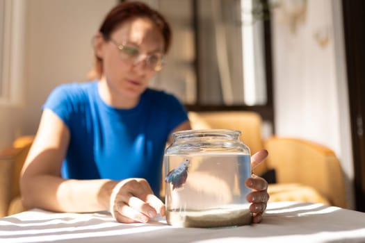 Woman admiring her betta fish swimming in a glass bowl placed on a table