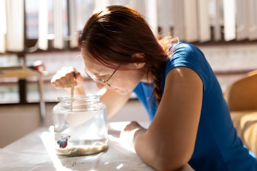 Young woman cleaning a fishbowl with a small net in a sunlit room