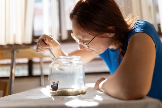 Woman carefully feeding her blue and red betta fish in a glass jar