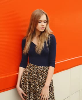 Beautiful young woman model with long blonde hair in leopard print skirt standing against red wall background, city street