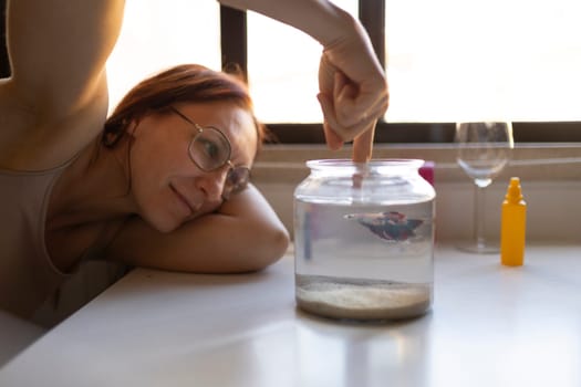 Woman interacting with her pet betta fish in a fishbowl, creating a peaceful and engaging moment