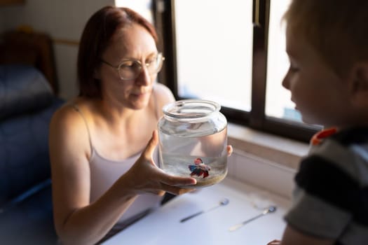 Mom holding a small fishbowl with a betta fish, teaching her son about aquatic life