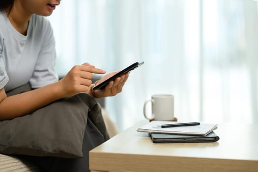 Smiling young woman browsing or texting on a smartphone, sitting on couch.