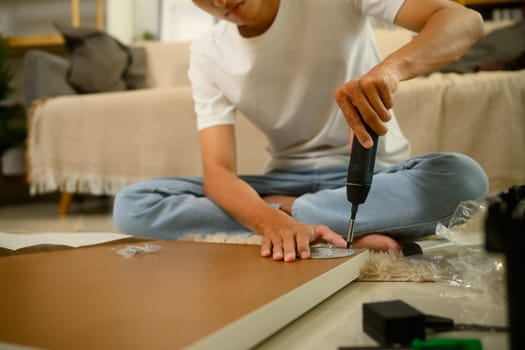 Focused Young homeowner assembling a new table, using a drill and tools to secure the legs.