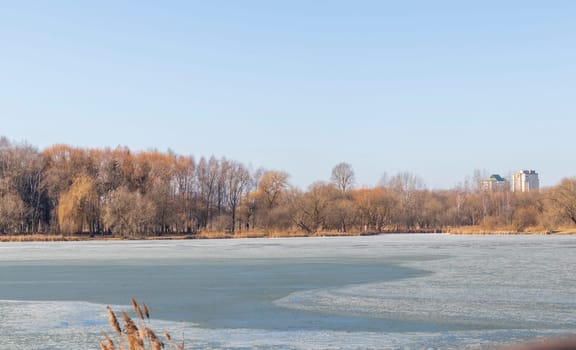 Lake covered with thawed ice, city on the background