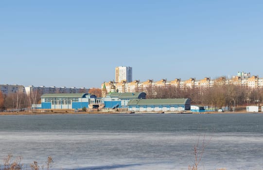 Lake covered with thawed ice, city on the background