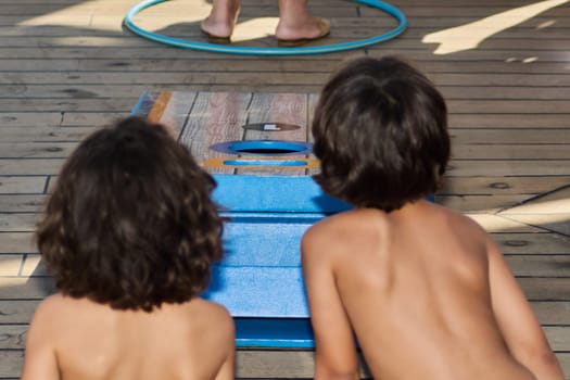 Catania. Italy - March 11, 2025: Teens actively participating and observing a cornhole match outdoors, capturing a moment of carefree recreational play and youthful joy.