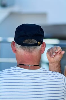 Man seen from behind, raising his hand in a relaxed setting, wearing a striped shirt and cap, with natural light enhancing the outdoor vibe.