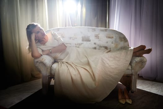 A middle-aged blonde woman poses gracefully on a vintage couch during a lifestyle blog photo shoot indoors.