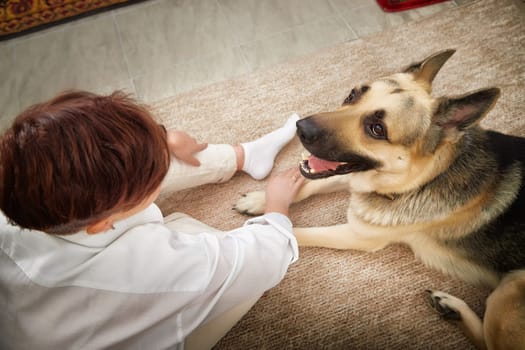 A blonde woman relaxes in a cozy room, sharing affectionate moments with her German Shepherd dog on a soft rug.