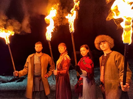 Actors perform a captivating fire show while dressed in ethnic costumes during a frosty winter night, showcasing their bravery and strength.