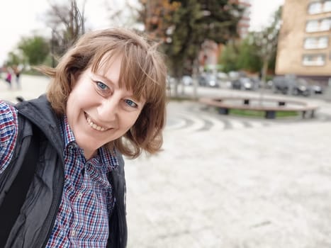 A middle-aged female blogger enjoys a sunny day, taking a selfie while exploring the vibrant city landscape.