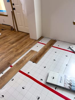 Broomfield, Colorado, USA-February 22, 2025-A home flooring installation project in progress, featuring wood laminate planks being laid over an underlayment. The partially completed floor shows the transition between the underlayment and installed planks. Construction tools and materials are visible in the background, highlighting a home renovation effort.