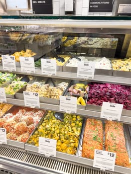 Castle Rock, Colorado, USA-February 22, 2025-A well-stocked Whole Foods deli case displaying a variety of fresh, prepared foods. The selection includes side dishes such as roasted vegetables, pasta salads, coleslaw, and other gourmet deli offerings. Each tray is labeled with pricing and descriptions, providing convenient meal options for customers.
