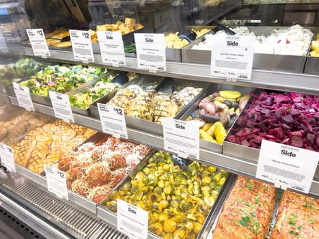 Castle Rock, Colorado, USA-February 22, 2025-A well-stocked Whole Foods deli case displaying a variety of fresh, prepared foods. The selection includes side dishes such as roasted vegetables, pasta salads, coleslaw, and other gourmet deli offerings. Each tray is labeled with pricing and descriptions, providing convenient meal options for customers.