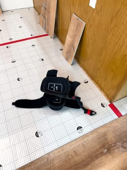 Broomfield, Colorado, USA-February 23, 2025-A kitchen undergoing flooring installation, with wood planks laid out against the wall and underlayment secured with red tape. The room features wooden cabinets, a light fixture, and a partially installed laminate or vinyl plank floor. Tools and materials are present, indicating an ongoing home renovation project.