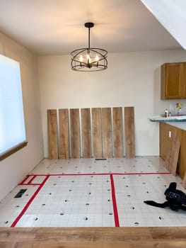 Broomfield, Colorado, USA-February 23, 2025-A kitchen undergoing flooring installation, with wood planks laid out against the wall and underlayment secured with red tape. The room features wooden cabinets, a light fixture, and a partially installed laminate or vinyl plank floor. Tools and materials are present, indicating an ongoing home renovation project.