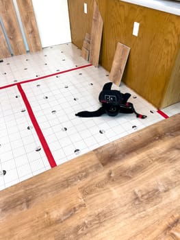 Broomfield, Colorado, USA-February 23, 2025-A kitchen undergoing flooring installation, with wood planks laid out against the wall and underlayment secured with red tape. The room features wooden cabinets, a light fixture, and a partially installed laminate or vinyl plank floor. Tools and materials are present, indicating an ongoing home renovation project.