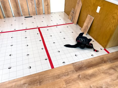 Broomfield, Colorado, USA-February 23, 2025-A kitchen undergoing flooring installation, with wood planks laid out against the wall and underlayment secured with red tape. The room features wooden cabinets, a light fixture, and a partially installed laminate or vinyl plank floor. Tools and materials are present, indicating an ongoing home renovation project.