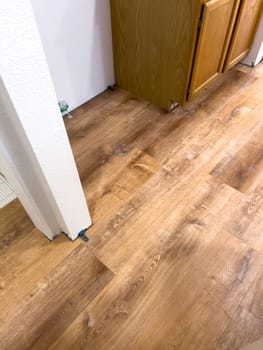Broomfield, Colorado, USA-February 23, 2025-A kitchen undergoing flooring installation, featuring newly laid wood planks extending through the space. The underlayment is partially visible, with red tape securing it. Wooden cabinets line the kitchen, and installation tools are placed on the floor, indicating an ongoing renovation project.