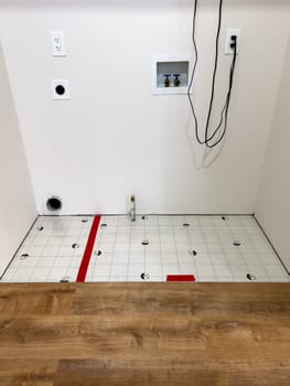 Broomfield, Colorado, USA-February 23, 2025-A kitchen undergoing flooring installation, featuring newly laid wood planks extending through the space. The underlayment is partially visible, with red tape securing it. Wooden cabinets line the kitchen, and installation tools are placed on the floor, indicating an ongoing renovation project.