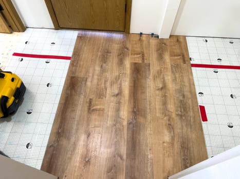Broomfield, Colorado, USA-February 23, 2025-A kitchen undergoing flooring installation, featuring newly laid wood planks extending through the space. The underlayment is partially visible, with red tape securing it. Wooden cabinets line the kitchen, and installation tools are placed on the floor, indicating an ongoing renovation project.