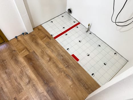 Broomfield, Colorado, USA-February 23, 2025-A kitchen undergoing flooring installation, featuring newly laid wood planks extending through the space. The underlayment is partially visible, with red tape securing it. Wooden cabinets line the kitchen, and installation tools are placed on the floor, indicating an ongoing renovation project.