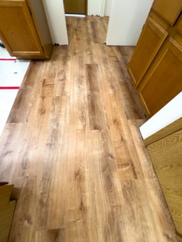 Broomfield, Colorado, USA-February 23, 2025-A kitchen with newly installed wood-look flooring, enhancing the space with a modern and warm aesthetic. The flooring extends through the room, complementing the wooden cabinetry. Some underlayment remains visible, indicating an ongoing home renovation project.