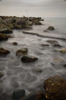 Soft waves gently lap against the rugged stones as twilight settles over the serene coastal landscape.