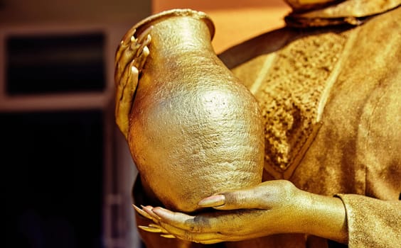 A golden-hued figure holds a beautifully crafted pot, radiating warmth and artistry in the afternoon sunlight, captivating all who pass by.