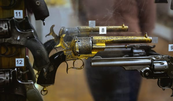 An array of antique revolvers, showcasing detailed craftsmanship, is exhibited behind glass in a vintage firearms shop.