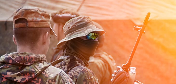 A group of soldiers dressed in camouflage is gearing up at a military camp, focused on their upcoming training drills.