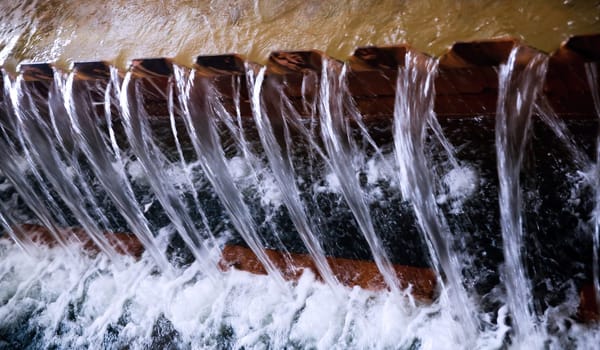 Water flows rapidly over the dam, creating gentle streams that glisten in the sunlight against a backdrop of calm waters.
