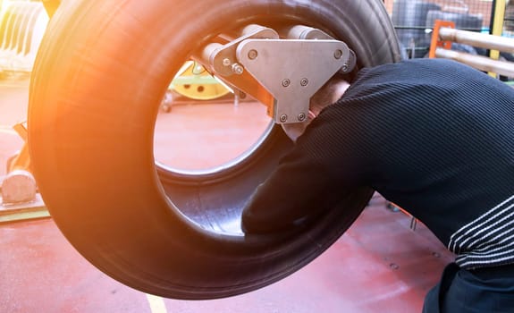 A skilled worker is focused on a large tire, adjusting equipment in a busy workshop environment filled with tools.