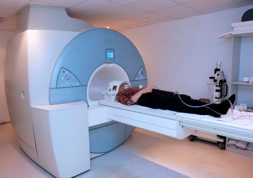 A patient lies on a scanning platform inside an MRI machine, surrounded by medical equipment in a healthcare setting.
