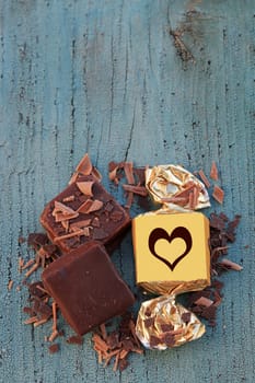 Viereckige Schokoladenpralinen mit Streusel und Goldpapier mit Herz auf einem Holzuntergrund
