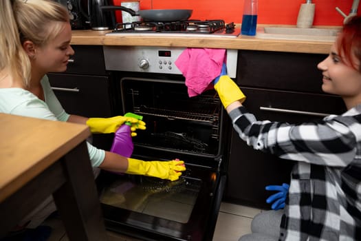 Two women are collaborating to clean an oven together, showcasing impressive teamwork in a bright and cheerful kitchen