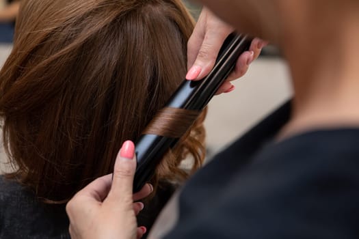 A stylist is expertly curling a clients hair with great precision by using an advanced flat iron technique