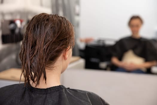 A person in a salon is waiting for their haircut, with wet hair and showcasing a vibrant beauty routine