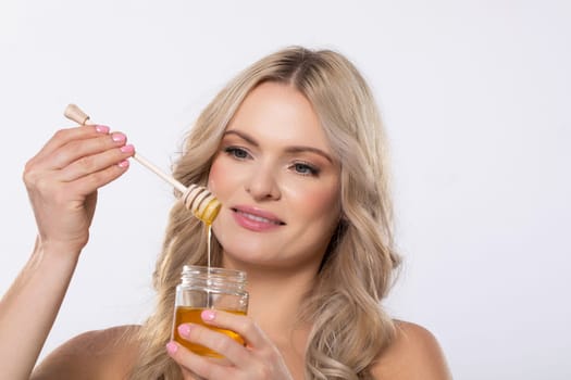 A woman smiles as she drizzles golden honey with a wooden dipper, showcasing the sweetness of this ingredient
