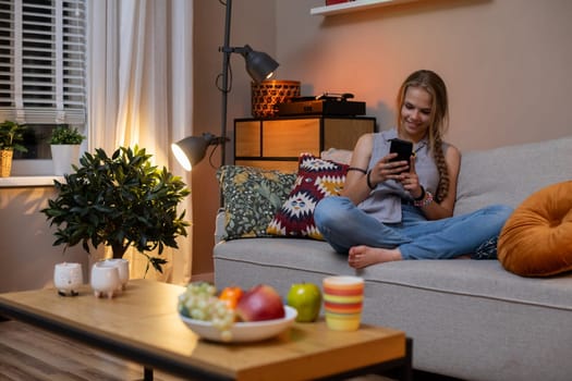 A serene indoor scene of a young woman relaxing on a couch, enjoying snacks and using her smartphone.