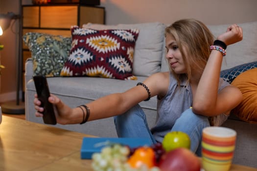A young woman sits at home, enjoying the moment and capturing it on her phone, with tasty snacks nearby
