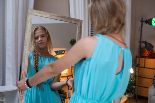 A girl in a turquoise dress gazes thoughtfully into a mirror, capturing a serene and peaceful moment