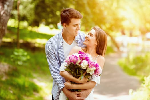 Young husband and wife with flower bouquet celebrating birthday outdoors on summer day