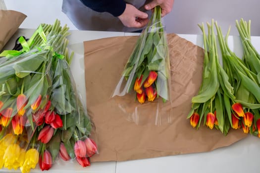 Florist arranging colorful tulip bouquets on wrapping paper.Top view