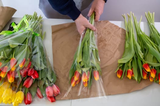 Caucasian male arranging tulips on craft paper: florist working with colorful flowers.Top view