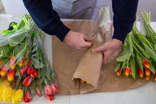 Male adult wrapping colorful tulips in brown paper bouquet arrangement.Top view