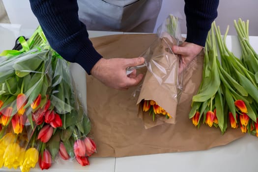Male florist wrapping tulips in shop with colorful bouquets and craft paper.Top view