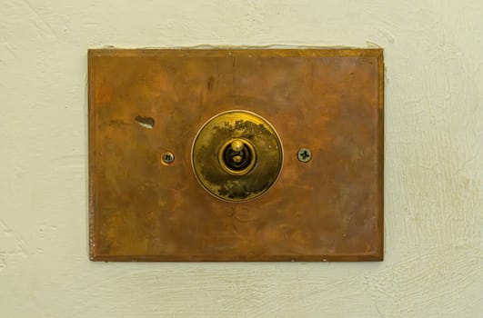 Close up of antique toggle light switch with copper faceplate on textured concrete wall providing vintage, rustic design detail.
